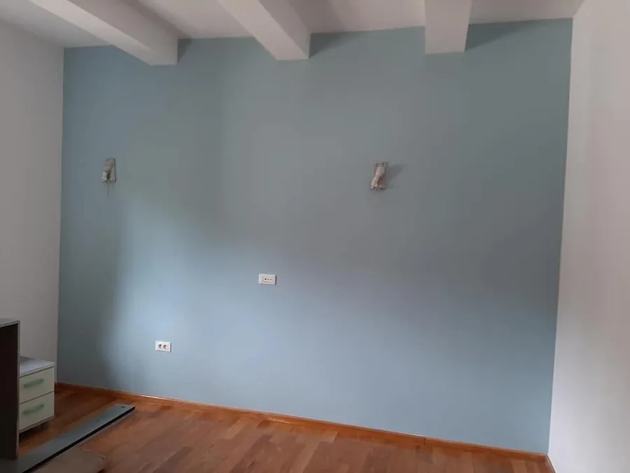 Pared azul claro bajo un techo con vigas blancas y junto a un suelo de madera