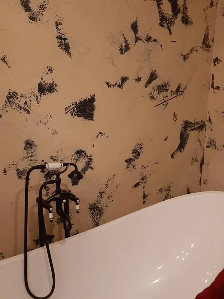 Bañera blanca, grifería negra y pared de acabado decorativo